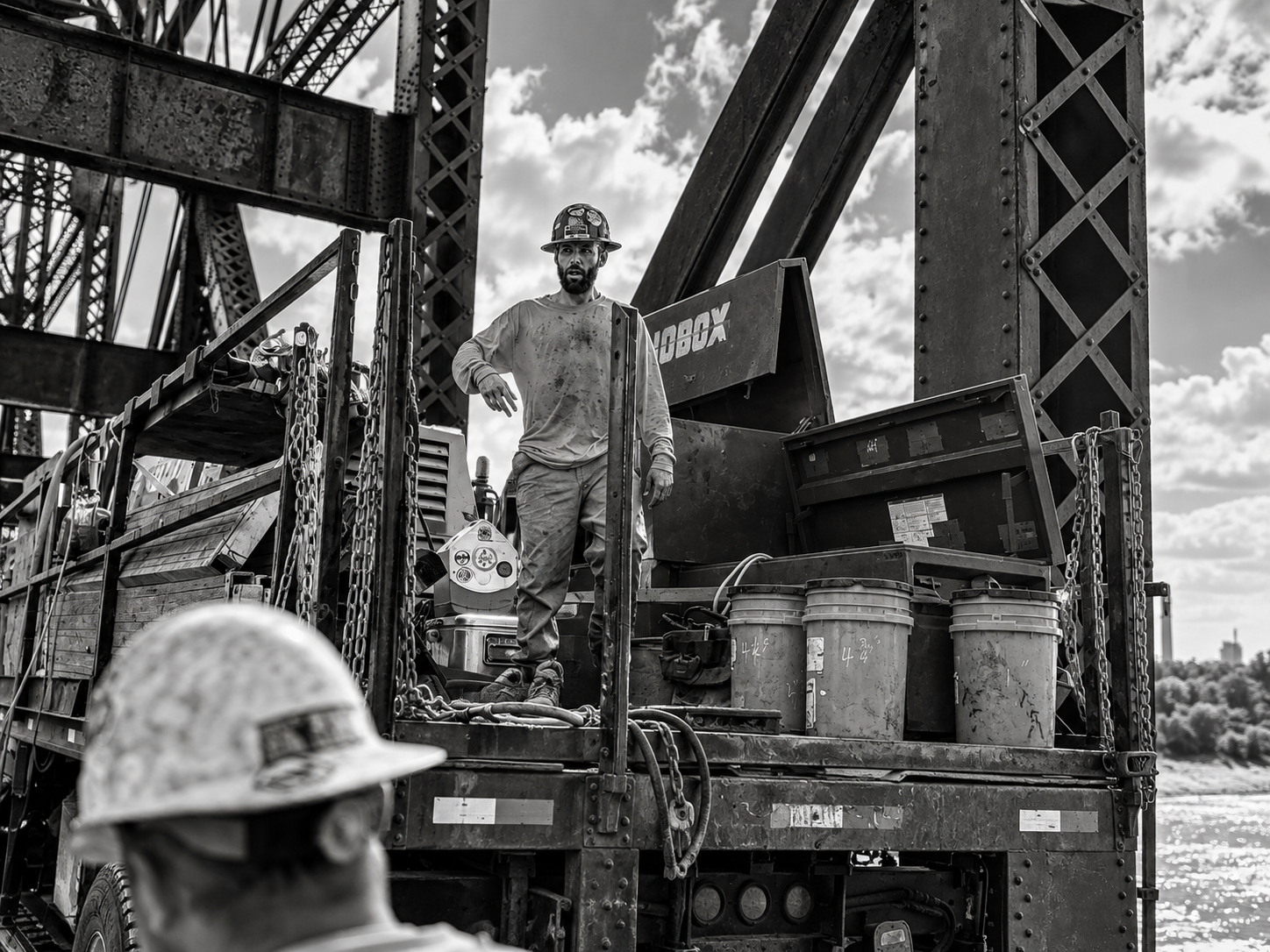 Ironworker on a work basket beside a steel truss bridge over the Mississippi River